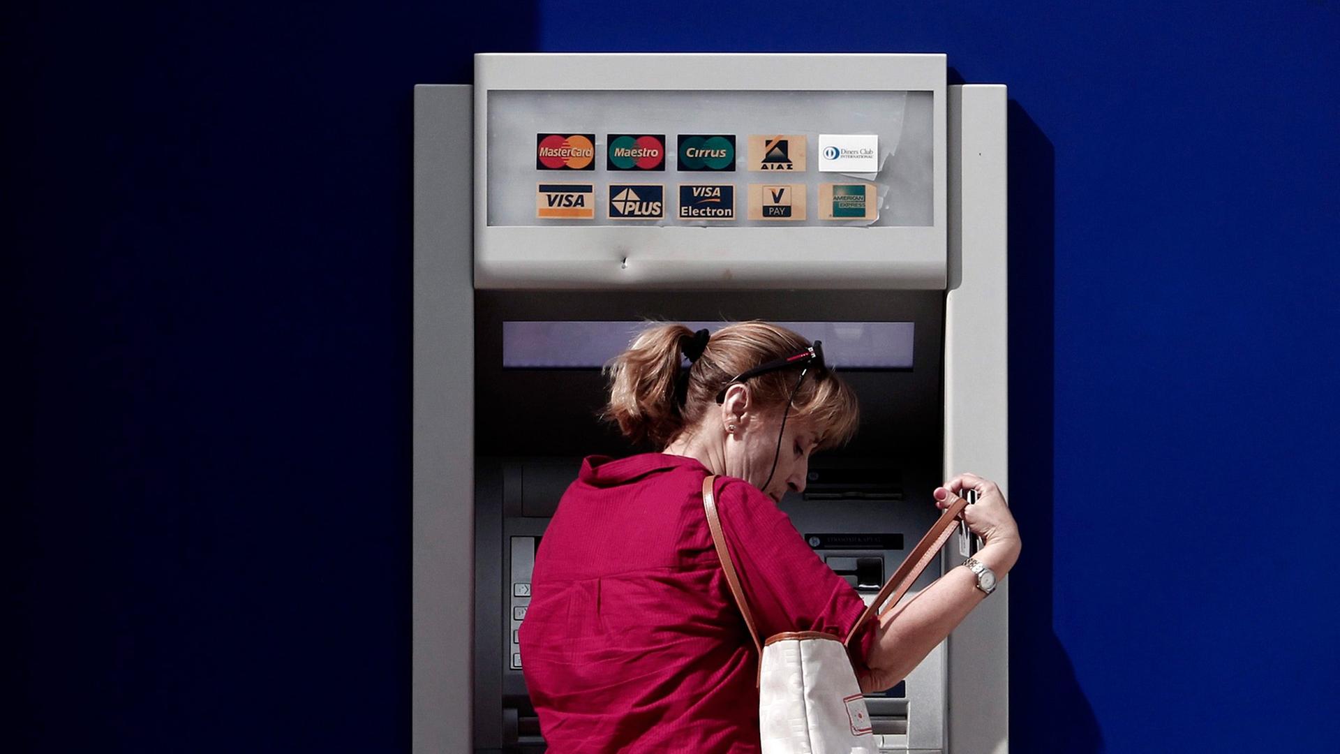 Eine Frau steht vor einem Geldautomaten der griechischen Eurobank.
