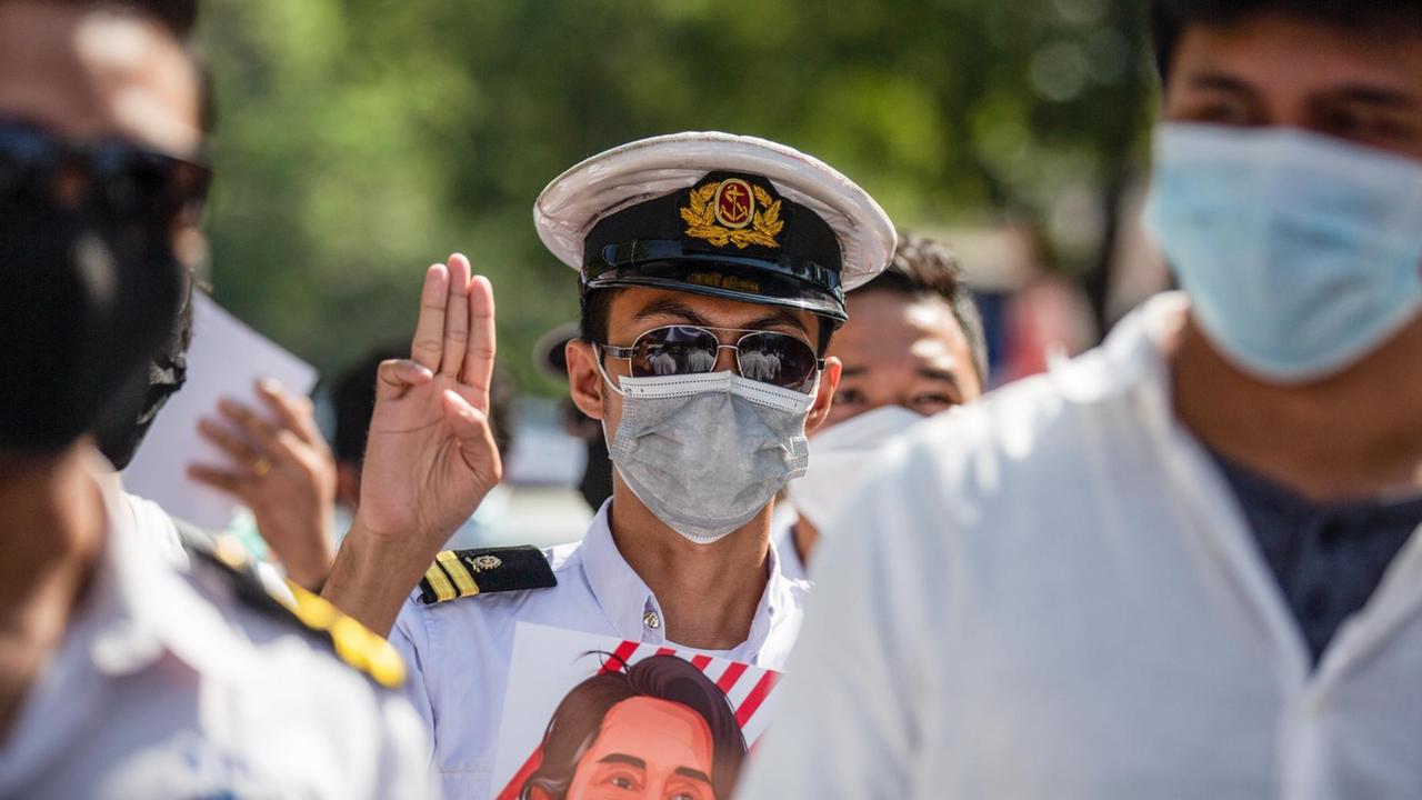 Ein Demonstrant zeigt den Dreifingergruß und trägt ein Bild von Aung San Suu Kyi beim Protest gegen den Militärputsch in Yangon, Myanmar am 12. Februar 2021 Ein Demonstrant zeigt den Dreifingergruß und trägt ein Bild von Aung San Suu Kyi beim Protest gegen den Militärputsch in Yangon, Myanmar am 12. Februar 2021