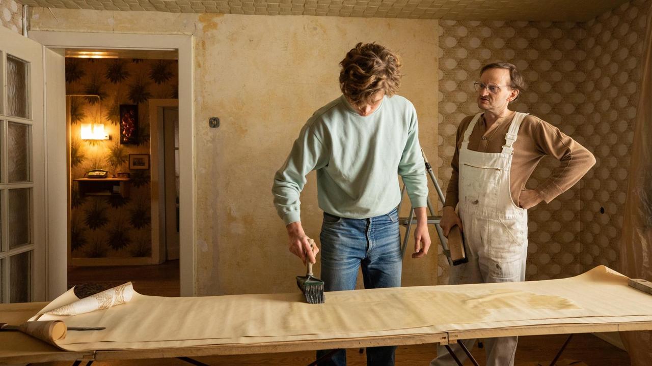 Szene aus dem Film "Auerhaus", einer der jungen Mitbewohner tapeziert einen Raum.