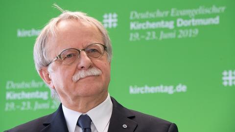 Hans Leyendecker steht vor einer grünen Wand, die den Kirchentag 2019 ankündigt.