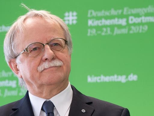 Hans Leyendecker steht vor einer grünen Wand, die den Kirchentag 2019 ankündigt.