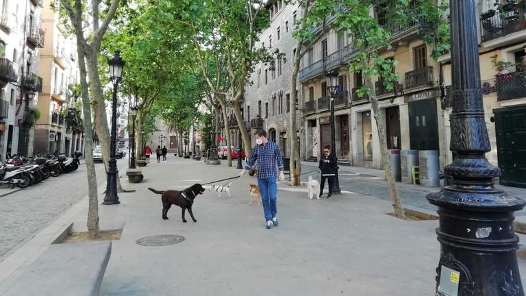Eine fast leere Fußgängerzone in Barcelona. Ein Mann geht mit eine Hund spazieren.