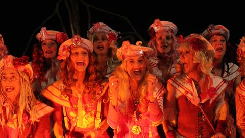 Die Frauen vom Chor "Die Brausen" aus Köln in bunten Kostümen, getaucht in rotes Licht.