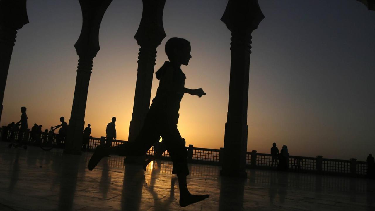 Ein Kind läuft vor untergehender Sonne an den Säulen einer Moschee vorbei. 
