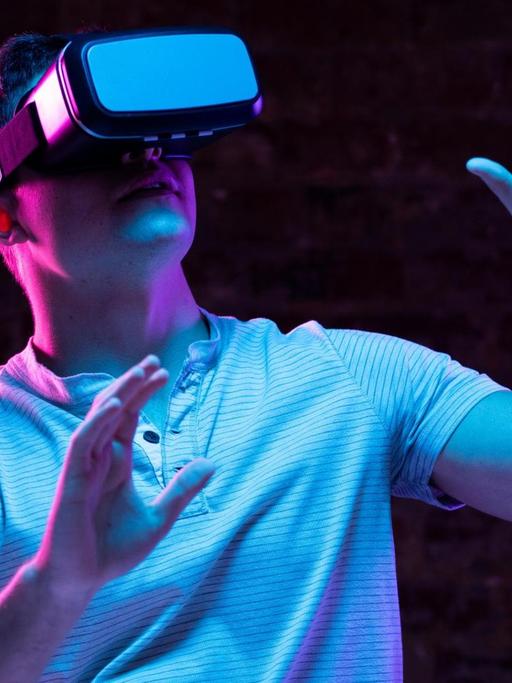 Ein Mann steht ein einem dunklen Raum trägt eine VR-Brille.