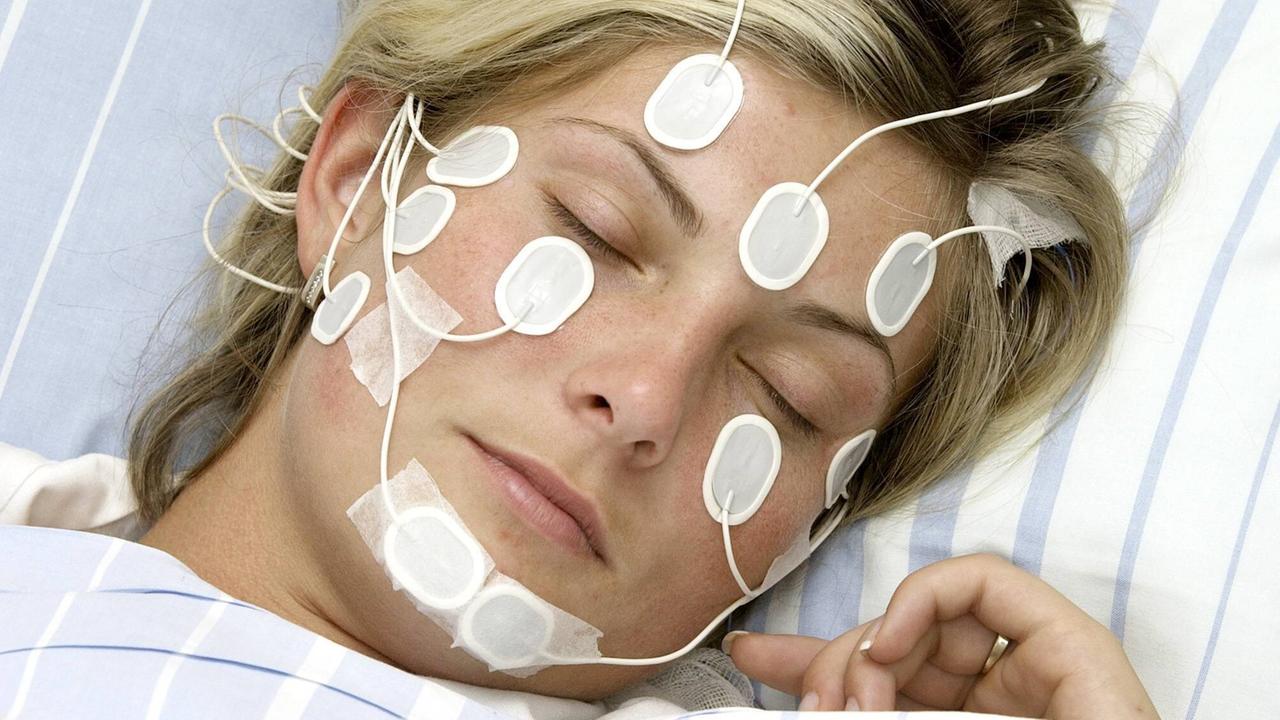 Eine Frau schläft im Schlaflabor mit angehefteten Elektroden im Gesicht. Eine Frau schläft im Schlaflabor mit angehefteten Elektroden im Gesicht.