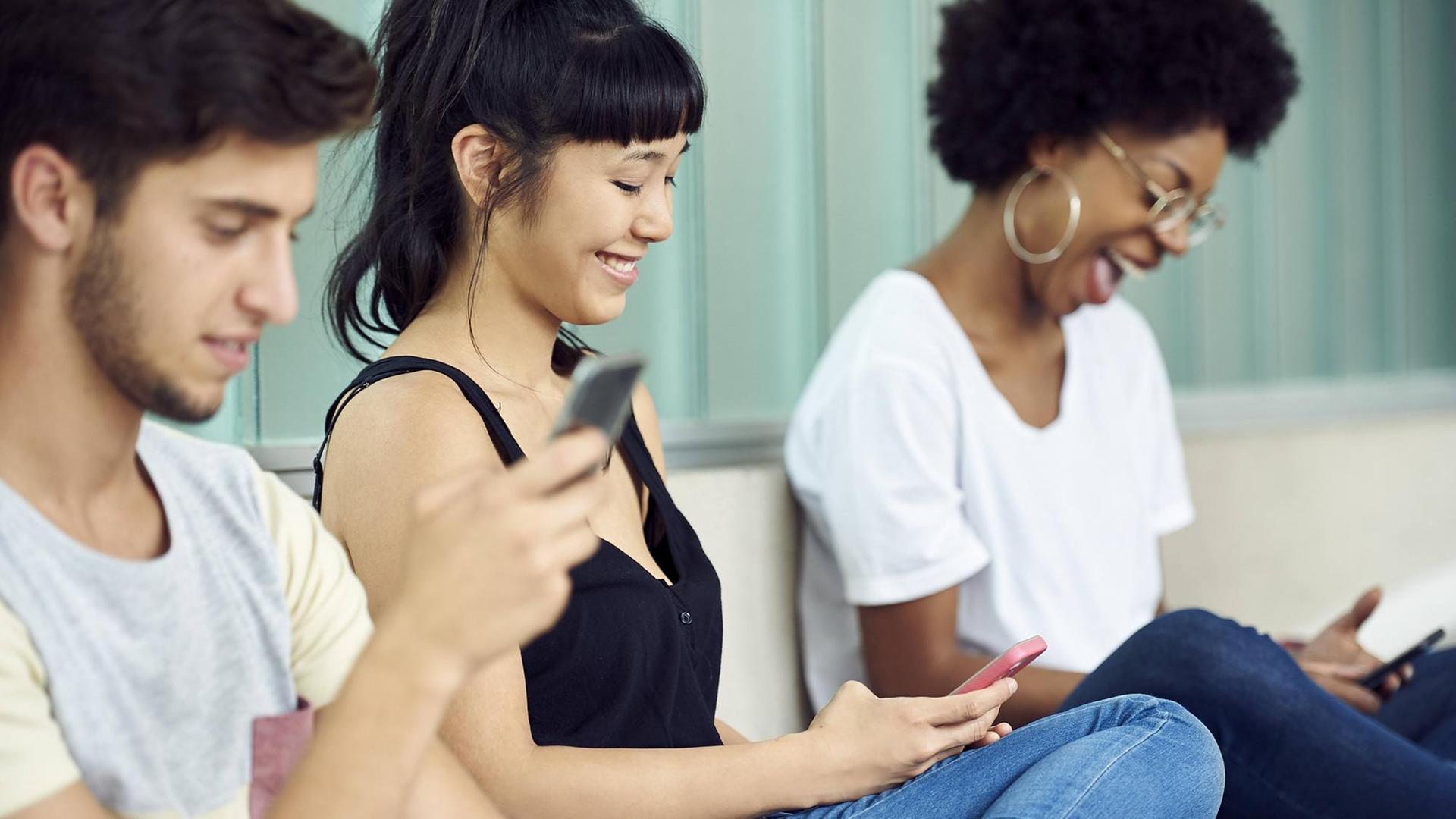 Drei junge Leute schauen auf ihre Smartphones. Drei junge Leute schauen auf ihre Smartphones.