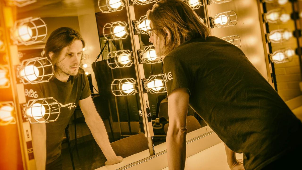 Ein Mann mit dünnen langen Haaren und Dreitagebarnt steht vor einem Spiegel. Ein Mann mit dünnen langen Haaren und Dreitagebarnt steht vor einem Spiegel.