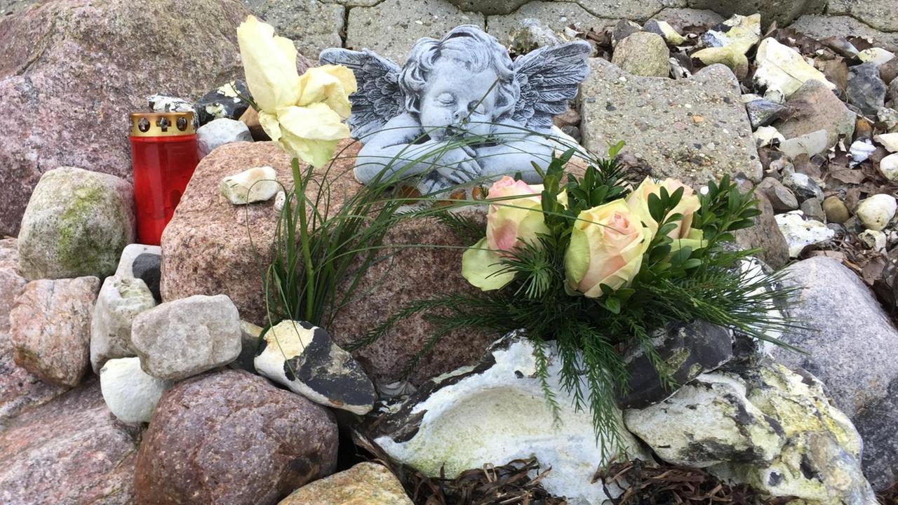 Kerzen, Blumen und eine Engelsfigur zwischen Muscheln und Sand Kerzen, Blumen und eine Engelsfigur zwischen Muscheln und Sand