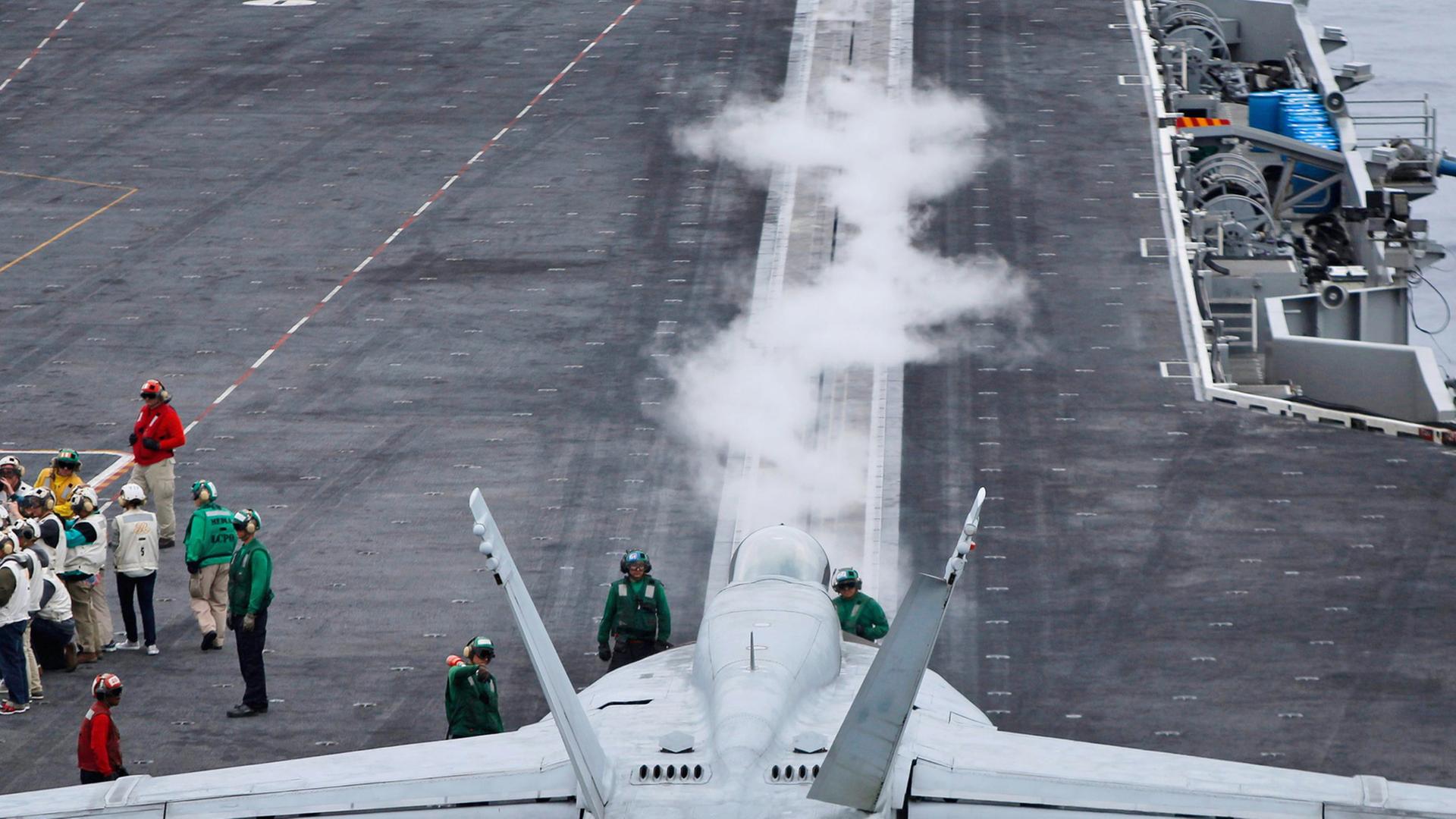 Auf dem Flugzeugträger "USS Ronald Reagan" steht ein Kampfjet, daneben sind einige Menschen zu sehen. Auf dem Flugzeugträger "USS Ronald Reagan" steht ein Kampfjet, daneben sind einige Menschen zu sehen.