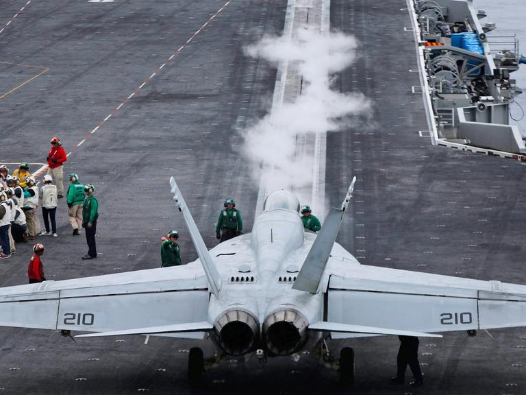 Auf dem Flugzeugträger "USS Ronald Reagan" steht ein Kampfjet, daneben sind einige Menschen zu sehen.