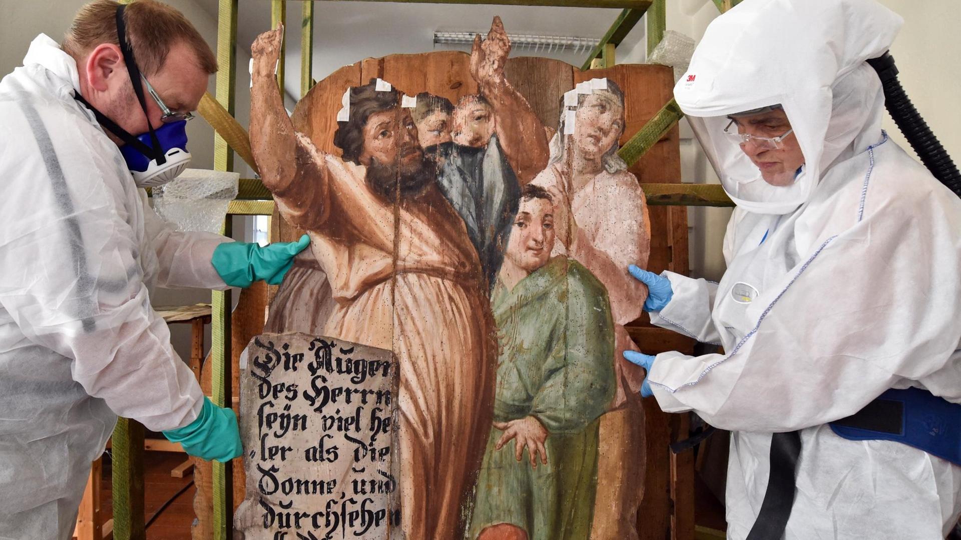 Zwei Restauratoren arbeiten unter Vollschutz mit Atemmasken an bemalten, historischen Holztafeln. Zwei Restauratoren arbeiten unter Vollschutz mit Atemmasken an bemalten, historischen Holztafeln.