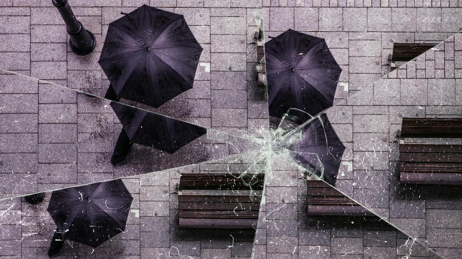 Bild einer Straße mit einem Mann unter einem schwarzen Regenschirm, aus der Vogelperspektive. Der Effekt eines zerbrochenen Spiegels ist über das Bild gelegt.