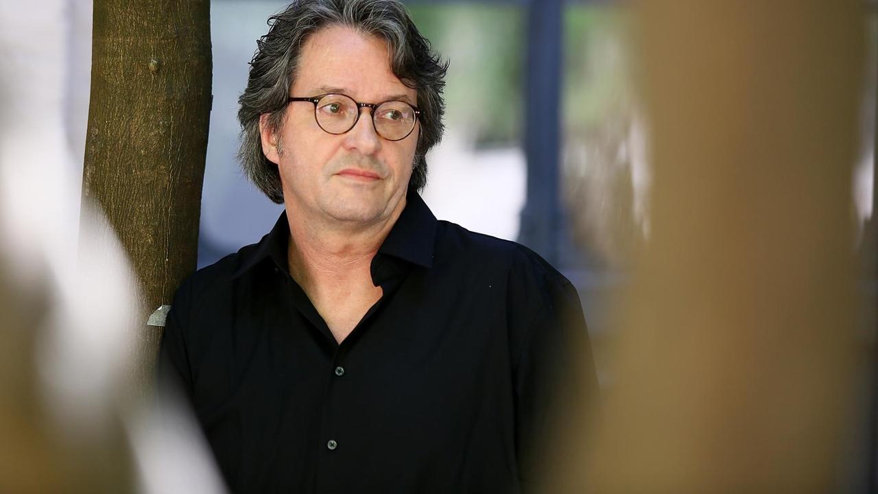 Ralf Rothmann lehnt an einen Baum und schaut zur Seite Ralf Rothmann lehnt an einen Baum und schaut zur Seite