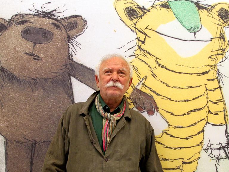 Illustrator und Geschichtenerzähler Janosch vor einem Plakat mit Bär, Tiger und Tigerente.