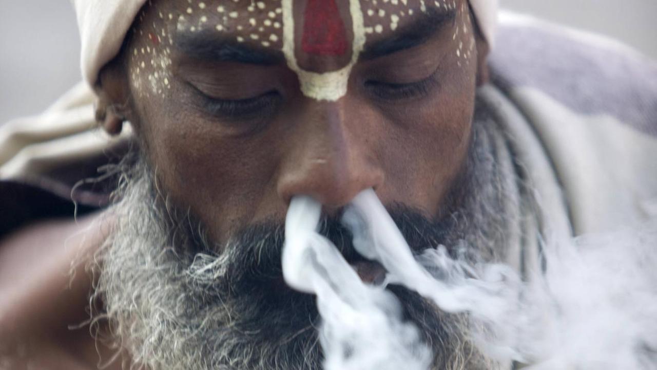 Einem Hindu Priester in Kathmandu, Nepal, strömt Rauch aus beiden Nasenlöchern. Einem Hindu Priester in Kathmandu, Nepal, strömt Rauch aus beiden Nasenlöchern.