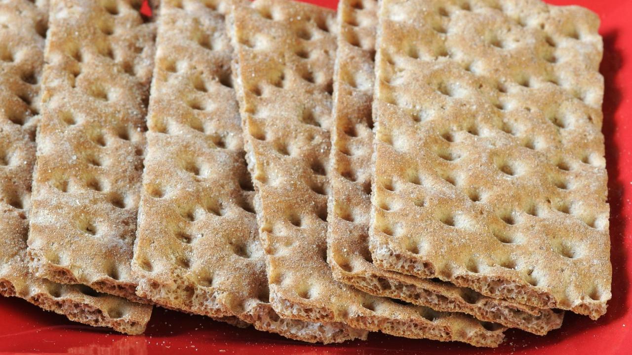 Mehrere Scheiben Knäckebrot liegen nebeneinander und aufeinander auf einer roten Unterlage. Mehrere Scheiben Knäckebrot liegen nebeneinander und aufeinander auf einer roten Unterlage.