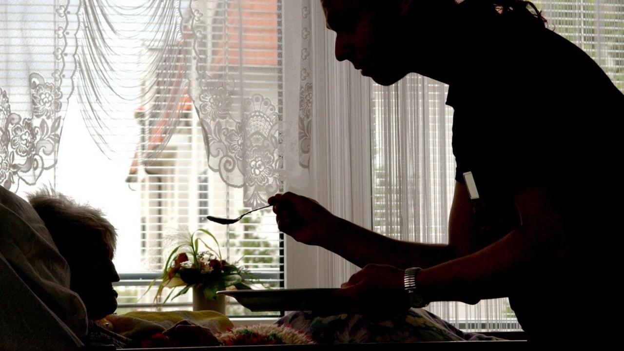 Eine Pflegerin reicht einer alten Frau Essen an