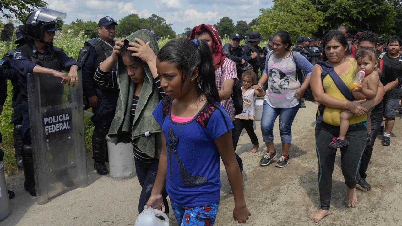 Das Foto zeigt Migranten auf dem Weg durch Mexiko, im Hintergrund die mexikanische Polizei.