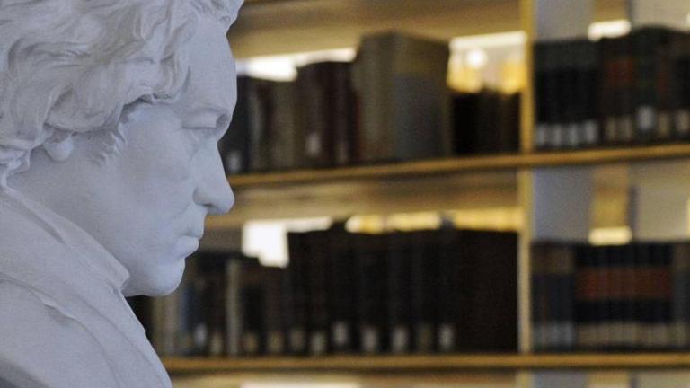 Blick auf eine weiße Beethoven-Büste, die scheinbar auf Regale voller alter Bücher blickt, die im Rokoko-Saal der Herzogin Anna Amalia Bibliothek in Weimar stehen.