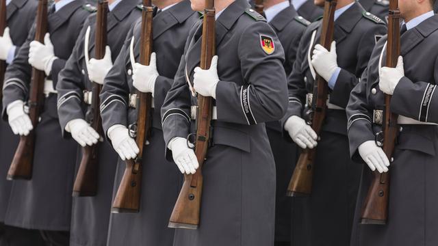 Detailaufnahme: Soldaten in grauen Mänteln mit Bundeswappen tragen weiße Handschuhe und Gewehre