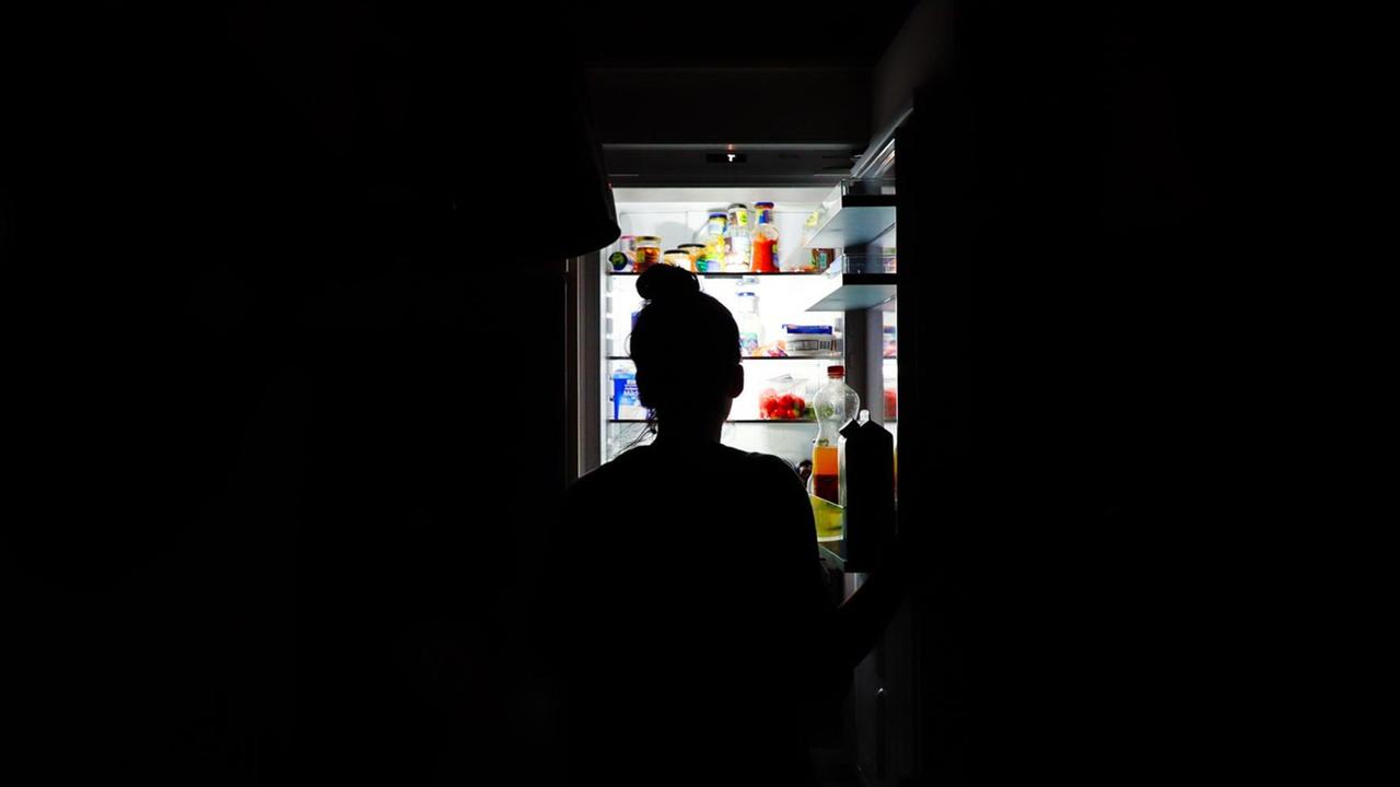 Silhouette einer Frau nachts vor dem offenen Kühlschrank. Silhouette einer Frau nachts vor dem offenen Kühlschrank.