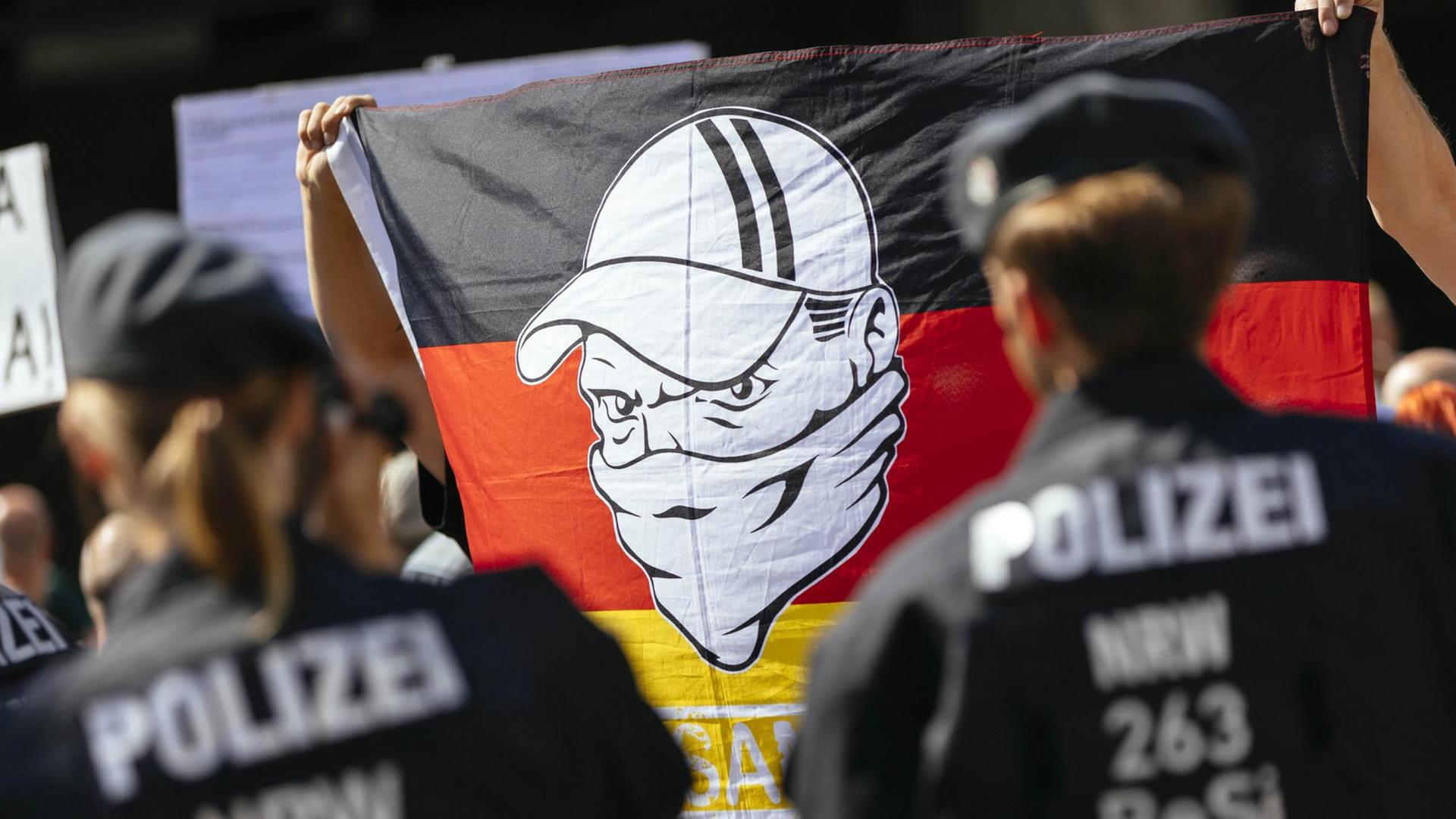 Rechtsorientierte Demonstranten bei einer Kundgebung im Bahnhofsviertel in Köln halten eine Deutschlandfahne hoch, auf der ein Mann mit Basecap und vermummtem Gesicht zu sehen ist, aufgenommen am 18.08.2018 Rechtsorientierte Demonstranten bei einer Kundgebung im Bahnhofsviertel in Köln halten eine Deutschlandfahne hoch, auf der ein Mann mit Basecap und vermummtem Gesicht zu sehen ist, aufgenommen am 18.08.2018