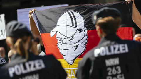 Rechtsorientierte Demonstranten bei einer Kundgebung im Bahnhofsviertel in Köln halten eine Deutschlandfahne hoch, auf der ein Mann mit Basecap und vermummtem Gesicht zu sehen ist, aufgenommen am 18.08.2018