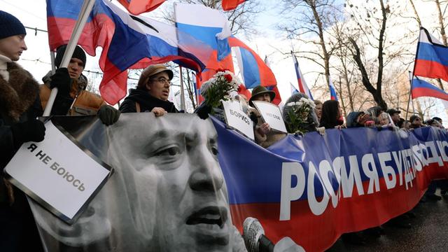 Demonstranten halten ein rot-blau-weißes Banner mit einem Bild von Boris Nemzow.