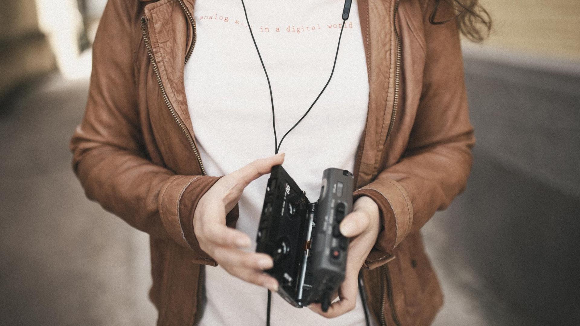 Eine Frau hält einen geöffneten Walkman in der Hand. Auf ihrem T-Shirt steht "analog in a digital world". Eine Frau hält einen geöffneten Walkman in der Hand. Auf ihrem T-Shirt steht "analog in a digital world".