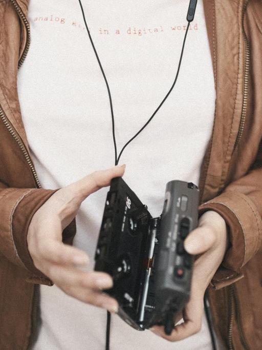 Eine Frau hält einen geöffneten Walkman in der Hand. Auf ihrem T-Shirt steht "analog in a digital world".