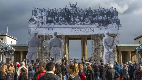 Der französische Street-Art-Künstler JR hat zum Tag der Deutschen Einheit 2018 eine Installation an das Brandenburger Tor heften lassen eine 25 Meter hohe, dreidimensionale Fotocollage. Die Aufnahmen stammen vom 10. November 1989, vom Tag nach dem Mauerfall.