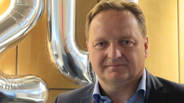 Jürgen Böhm, Landesvorsitzender Bayerischer Realschullehrerverband e.V. steht vor zwei silbernen Luftballons, die eine 20 darstellen.