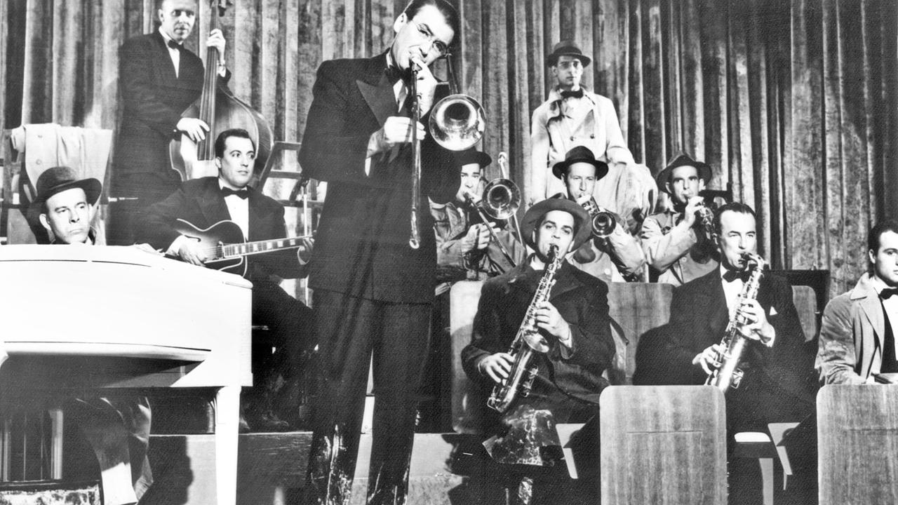 Glenn Millers weltbekannte Band, die in den späten Dreißiger und den frühen Vierziger Jahren Amerikas Spitzentanzorchester war – hier in einer Szene des biografischen Filmes "Die Glenn Miller Story" mit James Stewart (Mitte, mit Posaune) als Glenn Miller. Glenn Millers weltbekannte Band, die in den späten Dreißiger und den frühen Vierziger Jahren Amerikas Spitzentanzorchester war – hier in einer Szene des biografischen Filmes "Die Glenn Miller Story" mit James Stewart (Mitte, mit Posaune) als Glenn Miller.