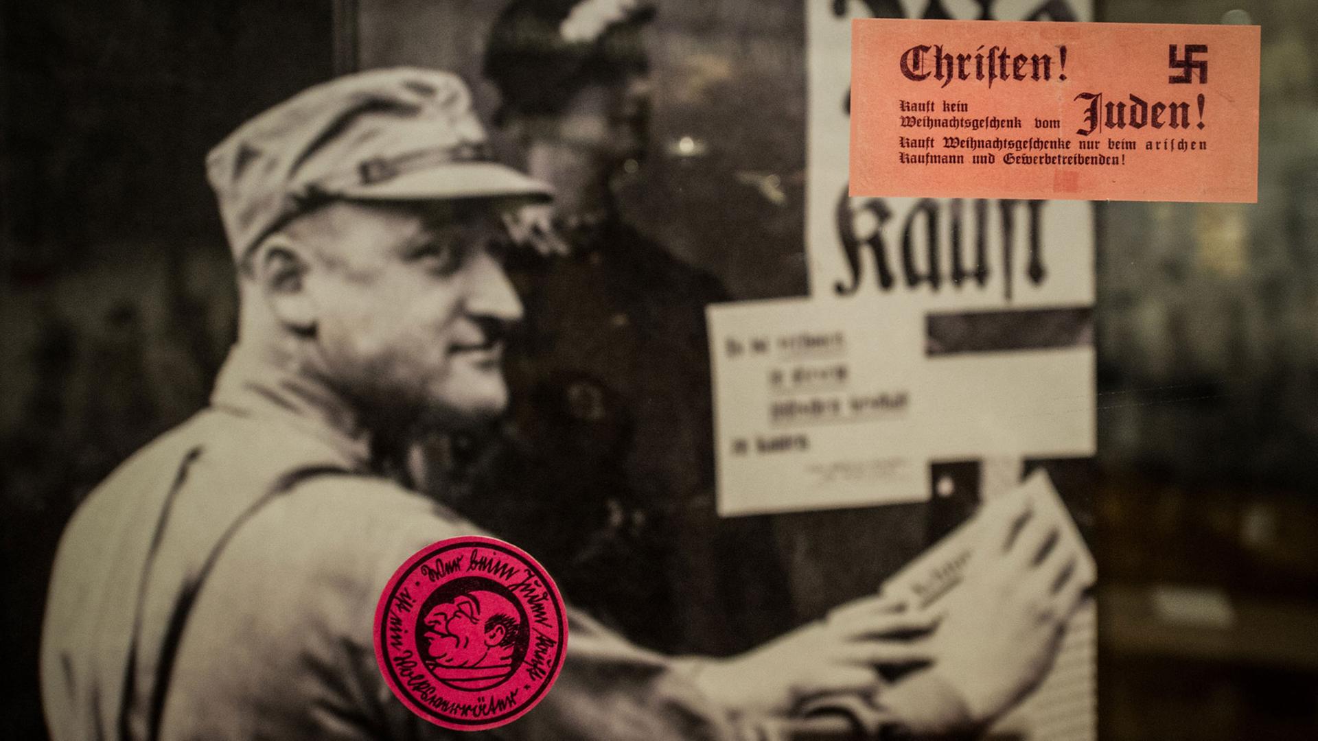 Sticker kleben am 19.04.2016 in Berlin im Rahmen der Ausstellung "Angezettelt Antisemitische und rassistische Aufkleber von 1880 bis heute" an einer Glasscheibe, hinter der auf einem Foto ein uniformierter Mann eine Wand beklebt. Die Ausstellung ist vom 20. April bis 31. Juli 2016 im Deutschen Historischen Museum zu sehen. Sticker kleben am 19.04.2016 in Berlin im Rahmen der Ausstellung "Angezettelt Antisemitische und rassistische Aufkleber von 1880 bis heute" an einer Glasscheibe, hinter der auf einem Foto ein uniformierter Mann eine Wand beklebt. Die Ausstellung ist vom 20. April bis 31. Juli 2016 im Deutschen Historischen Museum zu sehen.
