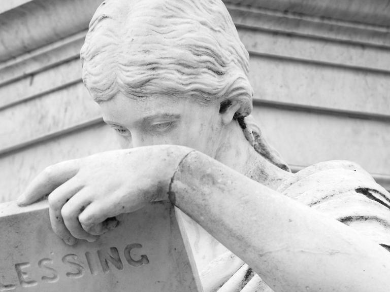 Eine Frauengestalt aus Marmor liest Lessing: Detail am Schillerdenkmal am Gendarmenmarkt in Berlin-Mitte