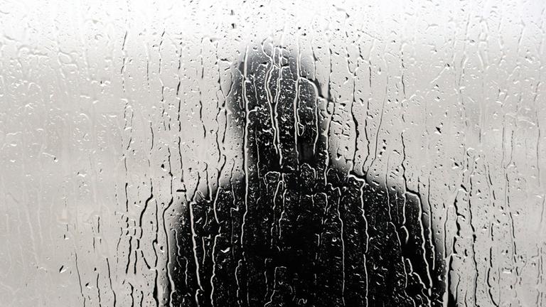 Ein Mann steht  im Regen hinter der Scheibe.