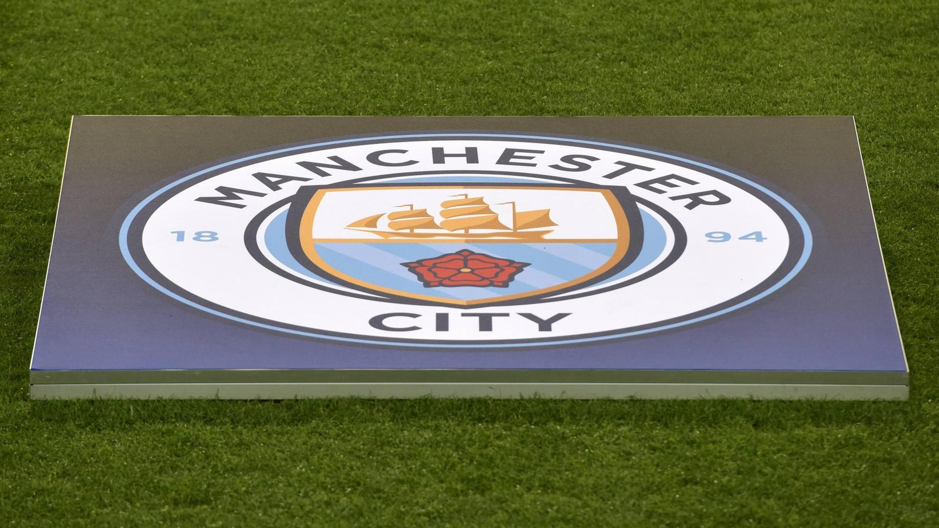 Das Bild zeigt das Logo des englischen Fußballvereins Manchester City. Es liegt im Stadion ausgebreitet auf dem Rasen. Das Bild zeigt das Logo des englischen Fußballvereins Manchester City. Es liegt im Stadion ausgebreitet auf dem Rasen.