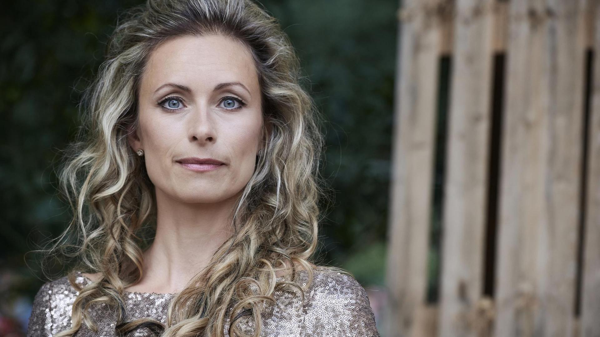 Eine Frau mit langen, blonden, lockigen Haaren schaut geradewegs in die Kamera. Eine Frau mit langen, blonden, lockigen Haaren schaut geradewegs in die Kamera.