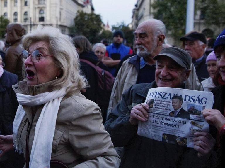 Mehrere Menschen vor dem Parlamentsgebäude in Ungarn, eine Frau ruft laut etwas, zwei halten eine Ausgabe der Zeitung Nepszabadsag.