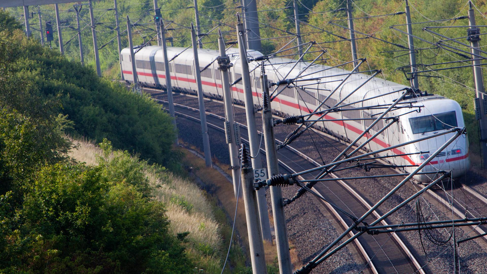 Ein Intercity Express Zug der Deutschen Bahn auf Fahrt in Hessen, im Vordergrund Masten und Oberleitungen.