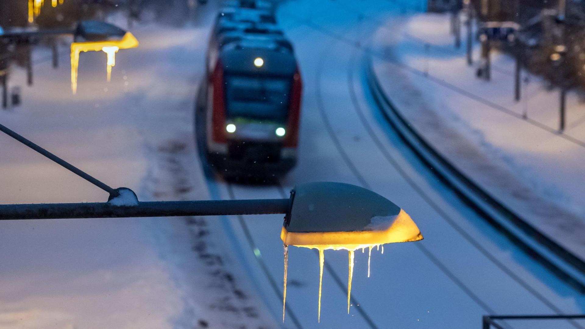 Eiszapfen hängen am frühen Morgen am verschneiten Bahnsteig am Bahnhof Signal-Iduna-Park an den Laternen, während eine Regionalbahn einfährt.