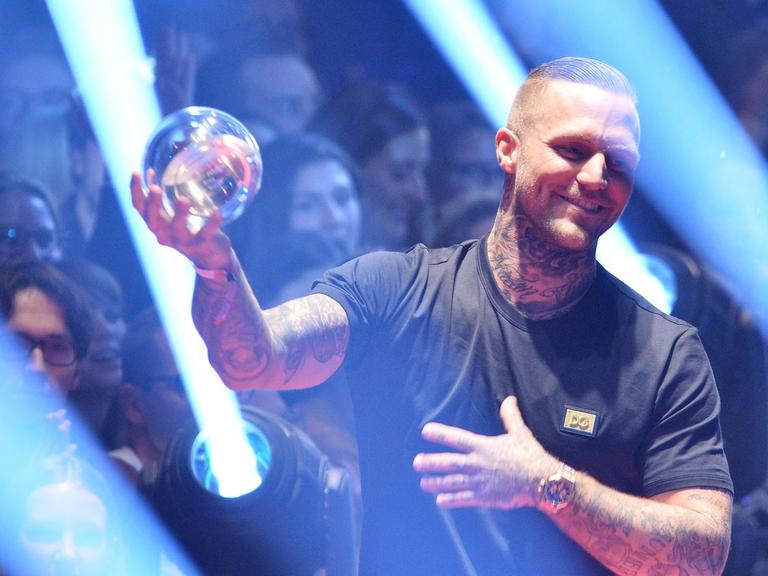 Kontra K steht im Lichtspiel auf der Bühne und zeigt den Pokal, eine Glaskugel.