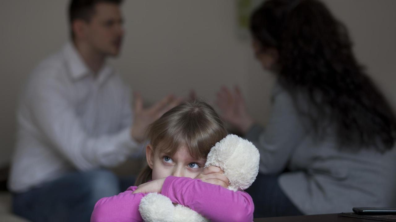 Zwei Erwachsene streiten sich in einer Wohnung, während die Tochter traurig ist (Symbolfoto). Zwei Erwachsene streiten sich in einer Wohnung, während die Tochter traurig ist (Symbolfoto).