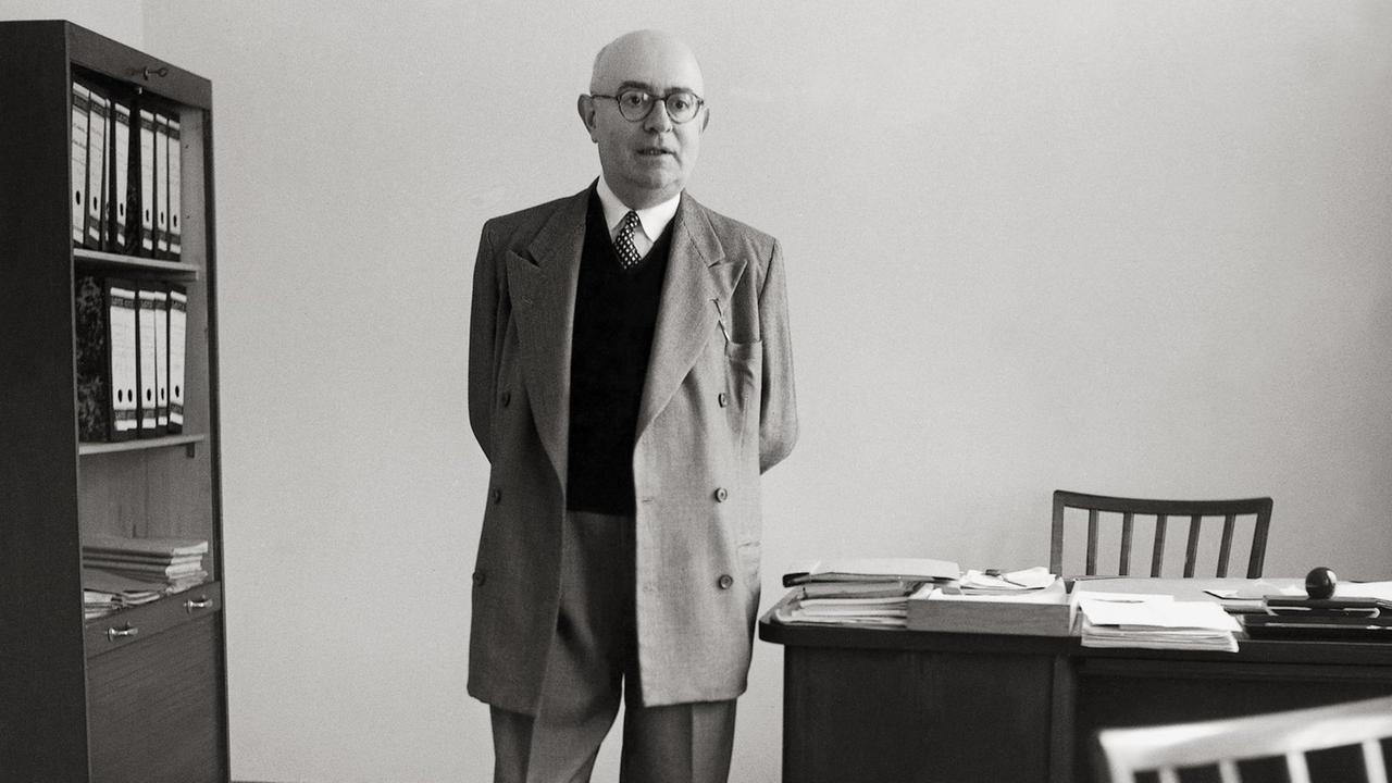 Adorno steht in seinem Büro am Schreibtisch.