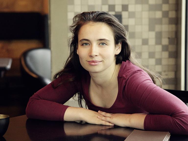 Porträt der Autorin Marina Frenk, sitzend an einem tisch, mit rotem Oberteil.