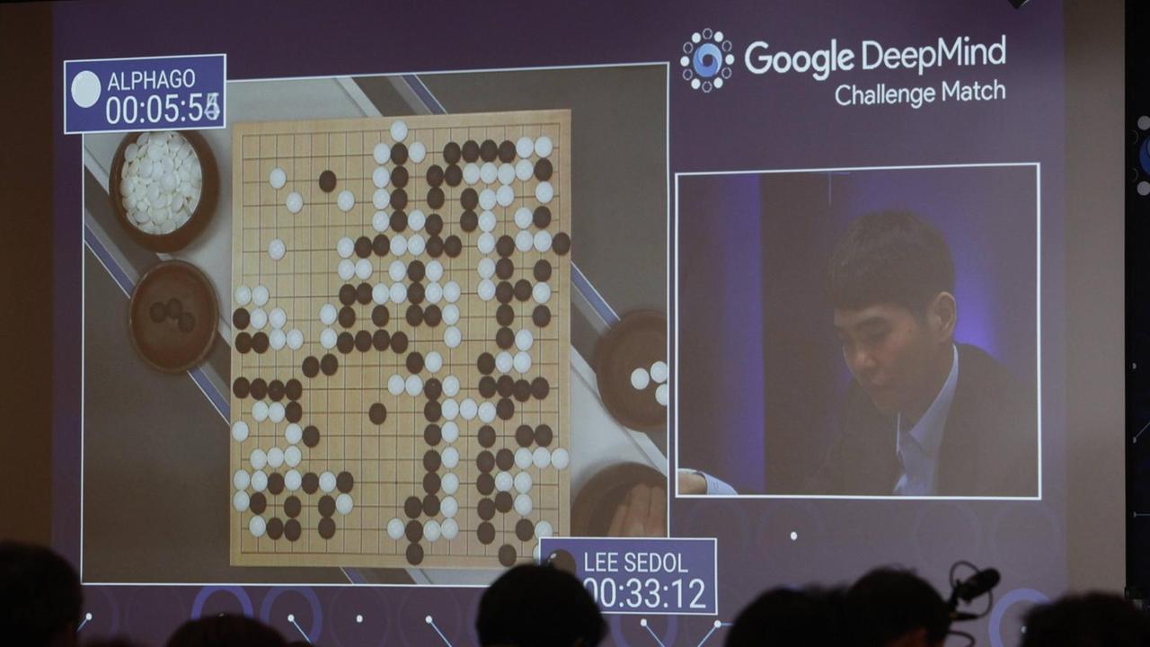 Man sieht einen Bildschirm, auf dem links ein Go-Brett und rechts der Spieler Lee Sedol zu sehen sind.