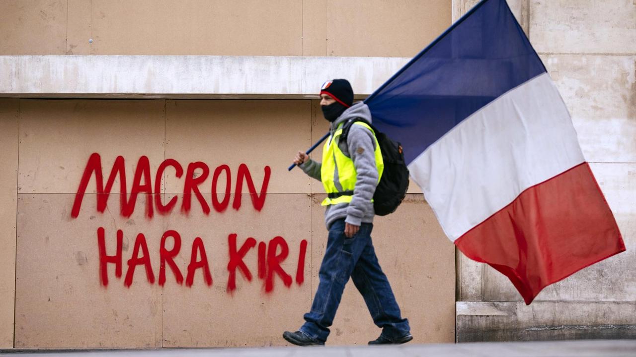 Ein Demonstrant der Gelb-Westen-Bewegung mit der französischen Fahne vor einer Mauer. Impression von den Gelbwesten-Protesten gegen Präsident Macron auf den Champs Elysées. Ein Demonstrant der Gelb-Westen-Bewegung mit der französischen Fahne vor einer Mauer. Impression von den Gelbwesten-Protesten gegen Präsident Macron auf den Champs Elysées.