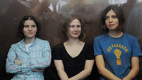 Drei Aktivistinnen der Band Pussy Riot sitzen nebeneinander auf einer Bank