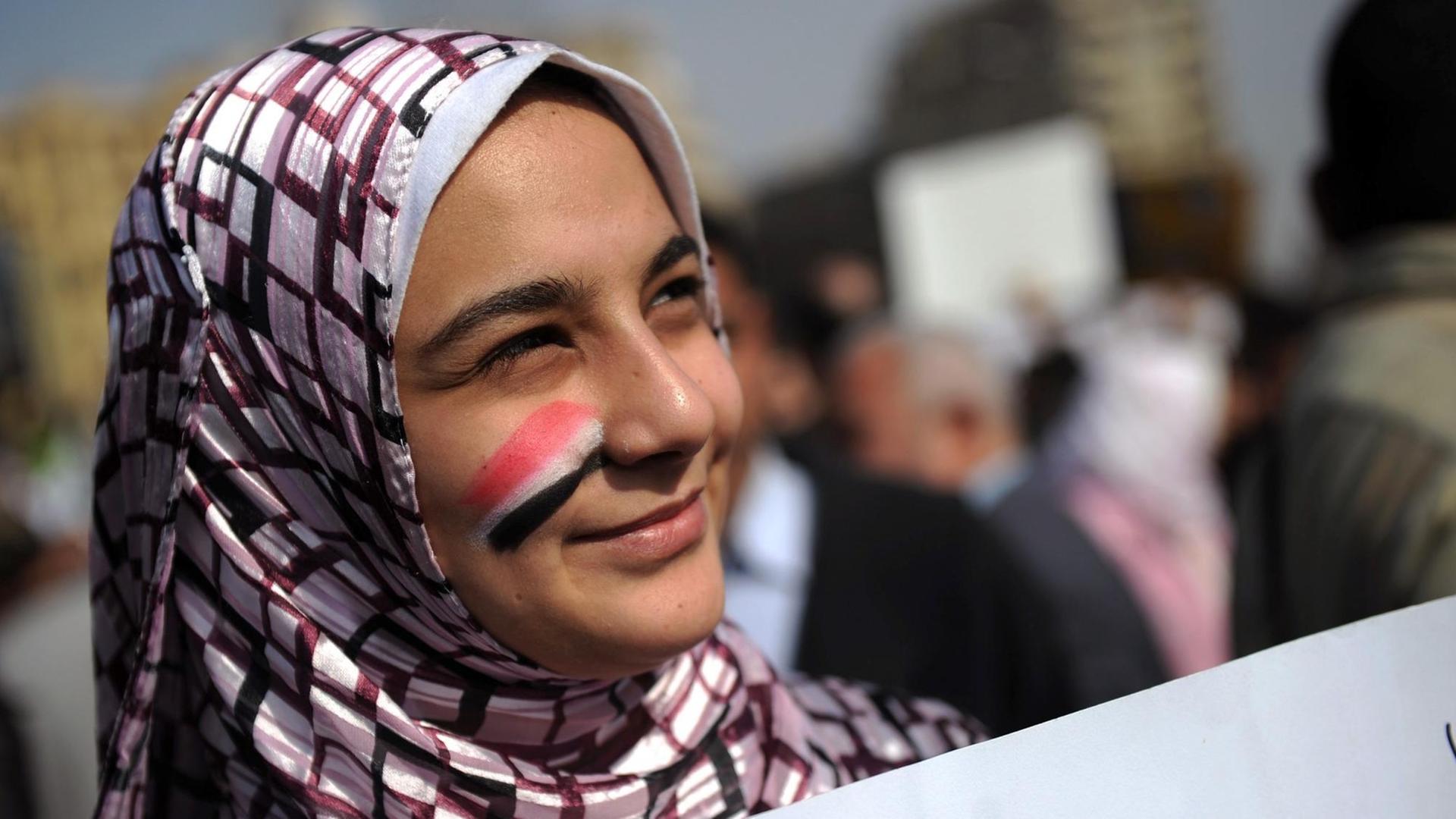 Eine junge Frau, die sich die ägyptischen Nationalfarben auf die Wange gemalt hat, steht mit einem Plakat inmitten der Demonstranten. Eine junge Frau, die sich die ägyptischen Nationalfarben auf die Wange gemalt hat, steht mit einem Plakat inmitten der Demonstranten.